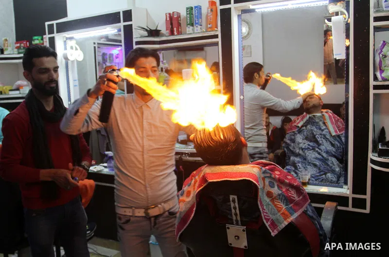 Ramadan Edwan, a Palestinian barber, uses fire in a hair-straightening technique with a client at his salon in the Rafah refugee camp, in the southern Gaza Strip on February 2, 2017. Photo by Abed Rahim Khatib