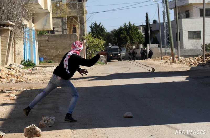 A Palestinian protester uses a slingshot to hurl stones towards Israeli security forces during clashes following a demonstration against the expropriation of Palestinian land by Israel in the village of Kfar Qaddum, near...