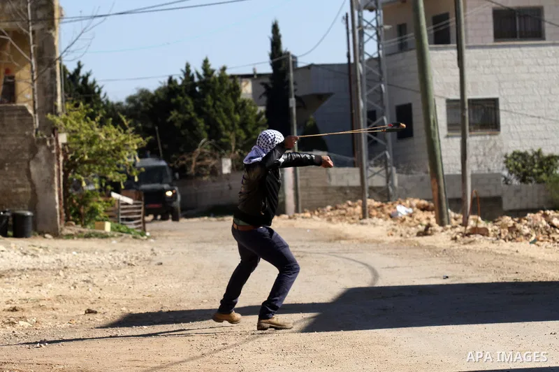 A Palestinian protester uses a slingshot to hurl stones towards Israeli security forces during clashes following a demonstration against the expropriation of Palestinian land by Israel in the village of Kfar Qaddum, near...