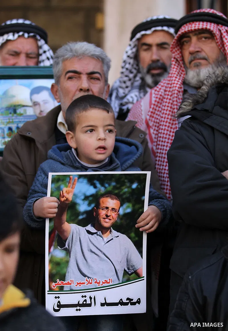 Palestinians hold posters bearing a portrait of Palestinian journalist Mohammed al-Qiq who is imprisoned in an Israeli jail during a protest in the West Bank city of Hebron, on February 10, 2017. Photo by Wisam Hashlamou...