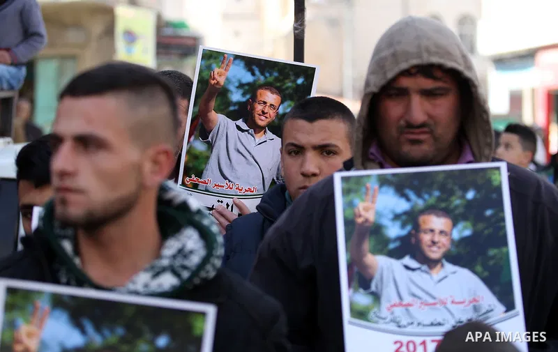 Palestinians hold posters bearing a portrait of Palestinian journalist Mohammed al-Qiq who is imprisoned in an Israeli jail during a protest in the West Bank city of Hebron, on February 10, 2017. Photo by Wisam Hashlamou...