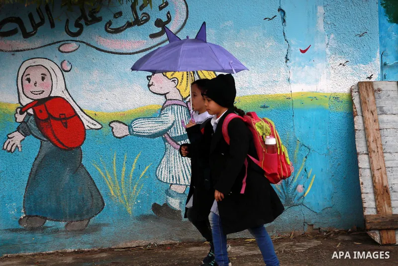 Palestinian students walk at street during a rainy day in Gaza City on February 14, 2017. Photo by Mohammed Asad