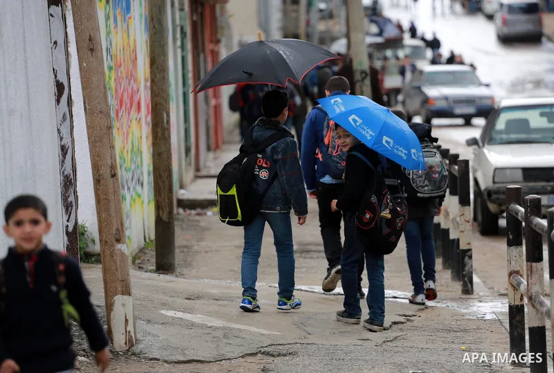 Palestinian students walk at street during a rainy day in Gaza City on February 14, 2017. Photo by Mohammed Asad