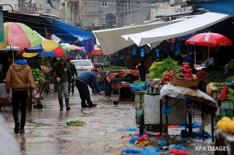 Palestinians walk through a wet street during a rainy day at a market at the Al-Shati refugee camp in Gaza City on February 14, 2017. Photo by Mohammed Asad