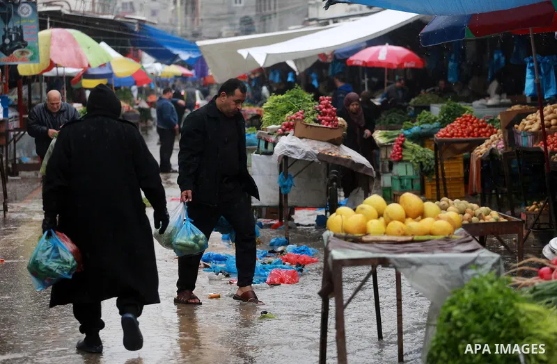 Palestinians walk through a wet street during a rainy day at a market at the Al-Shati refugee camp in Gaza City on February 14, 2017. Photo by Mohammed Asad