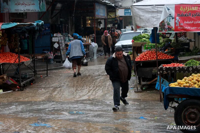Palestinians walk through a wet street during a rainy day at a market at the Al-Shati refugee camp in Gaza City on February 14, 2017. Photo by Mohammed Asad