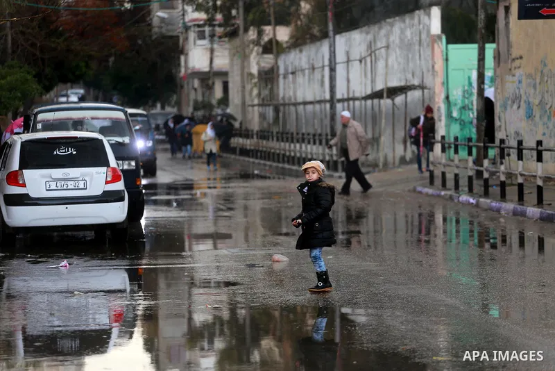 Palestinian students walk at a wet street during a rainy day in Gaza City on February 14, 2017. Photo by Mohammed Asad