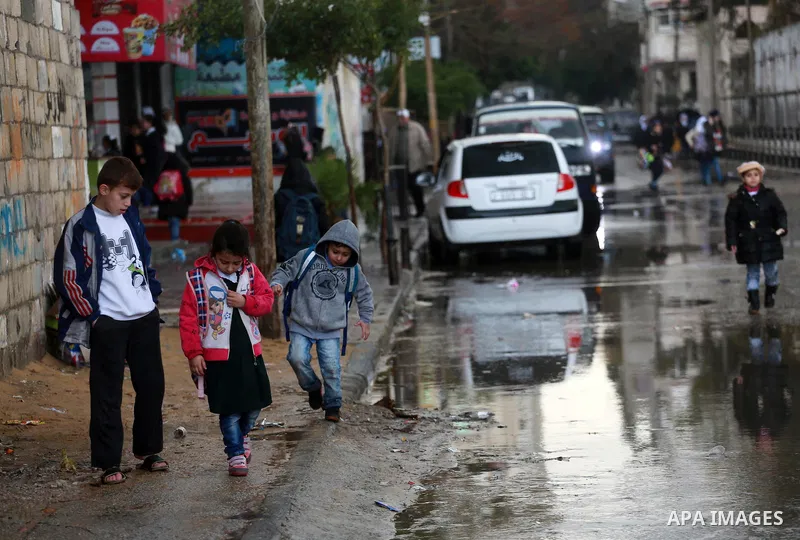 Palestinian students walk at a wet street during a rainy day in Gaza City on February 14, 2017. Photo by Mohammed Asad