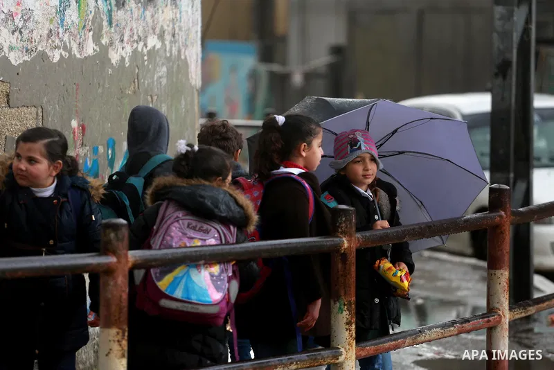 Palestinian students walk at street during a rainy day in Gaza City on February 14, 2017. Photo by Mohammed Asad