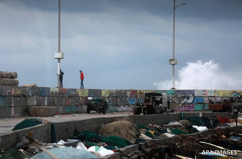 Palestinians stand on wall at the Gaza seaport during a rainy day in Gaza City on February 14, 2017. Photo by Mohammed Asad