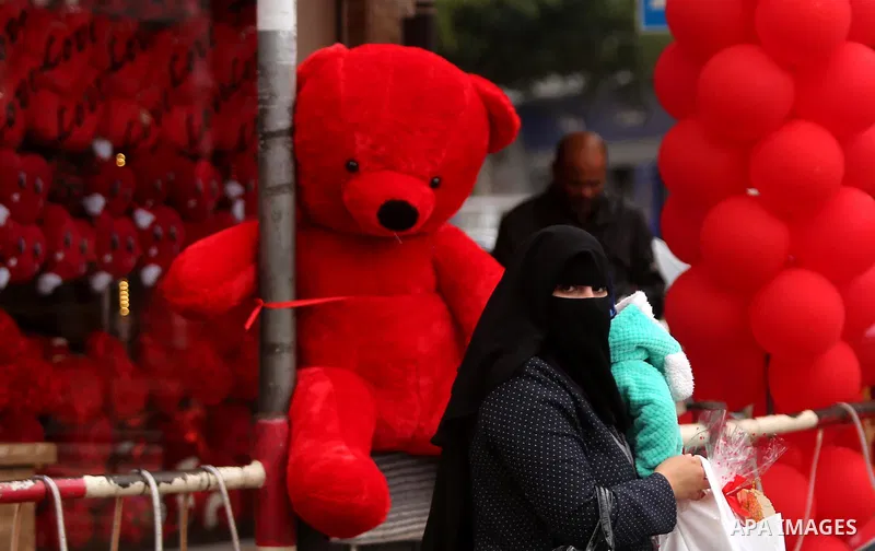 Palestinians walk past a shop selling red teddy bears, red ballons and pillows on Valentine's day in Gaza city on February 14, 2017. Valentine's Day is increasingly popular in the region as people have taken up the custo...