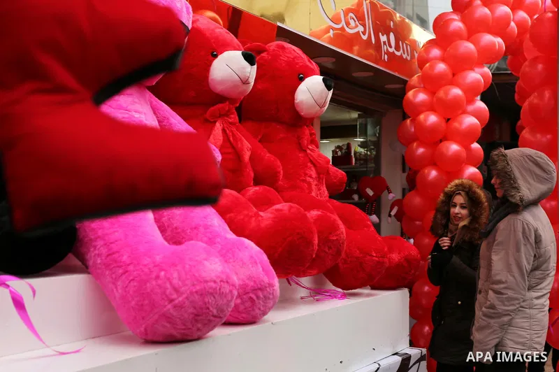Palestinians walk past a shop selling red teddy bears, red ballons and pillows on Valentine's day in Gaza city on February 14, 2017. Valentine's Day is increasingly popular in the region as people have taken up the custo...