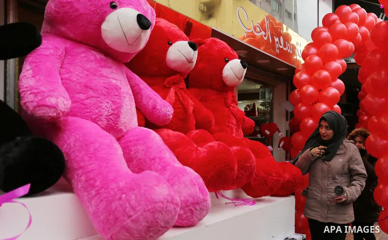 Palestinians walk past a shop selling red teddy bears, red ballons and pillows on Valentine's day in Gaza city on February 14, 2017. Valentine's Day is increasingly popular in the region as people have taken up the custo...