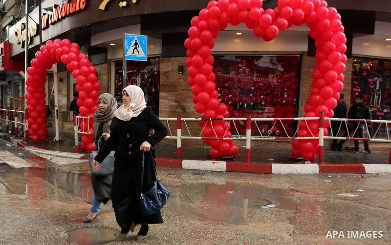 Palestinians walk past a shop selling red teddy bears, red ballons and pillows on Valentine's day in Gaza city on February 14, 2017. Valentine's Day is increasingly popular in the region as people have taken up the custo...