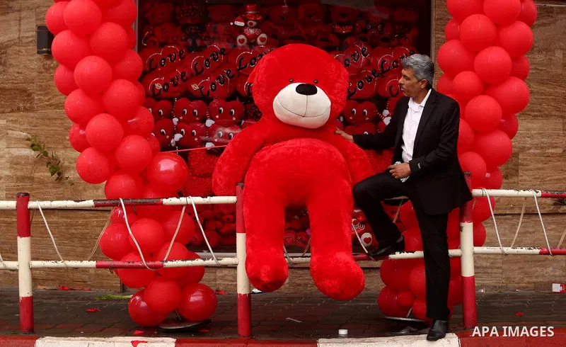 Palestinians walk past a shop selling red teddy bears, red ballons and pillows on Valentine's day in Gaza city on February 14, 2017. Valentine's Day is increasingly popular in the region as people have taken up the custo...