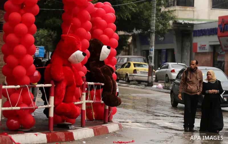 Palestinians walk past a shop selling red teddy bears, red ballons and pillows on Valentine's day in Gaza city on February 14, 2017. Valentine's Day is increasingly popular in the region as people have taken up the custo...