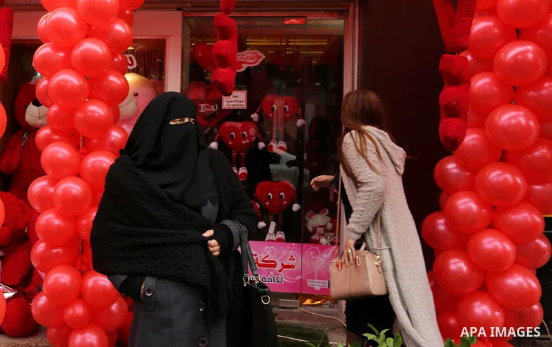 Palestinians walk past a shop selling red teddy bears, red ballons and pillows on Valentine's day in Gaza city on February 14, 2017. Valentine's Day is increasingly popular in the region as people have taken up the custo...