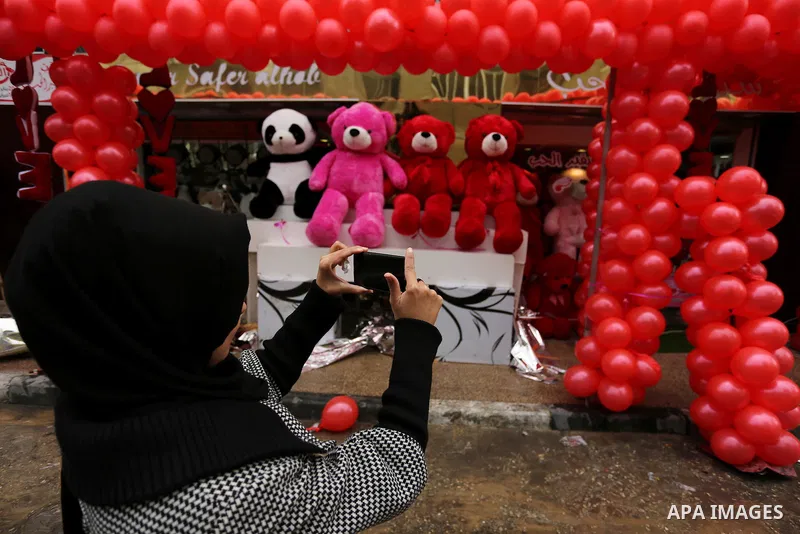 A Palestinian woman uses her mobile phone to take a photo for red teddy bears outside a shop on Valentine's day in Gaza city on February 14, 2017. Valentine's Day is increasingly popular in the region as people have take...