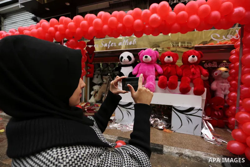A Palestinian woman uses her mobile phone to take a photo for red teddy bears outside a shop on Valentine's day in Gaza city on February 14, 2017. Valentine's Day is increasingly popular in the region as people have take...
