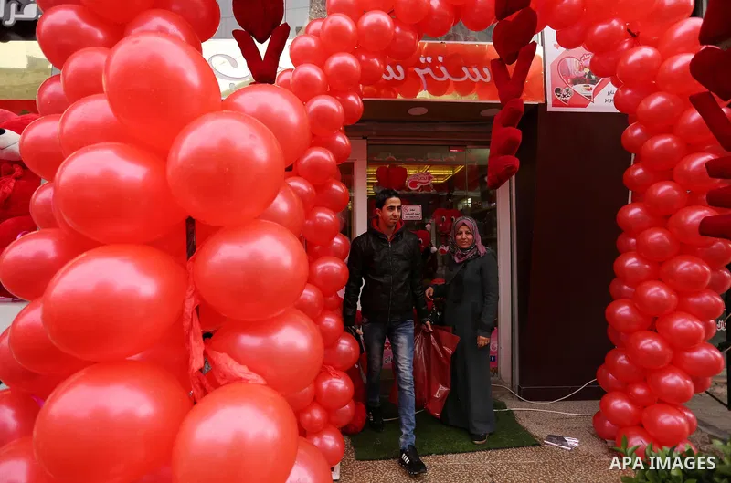 Palestinians walk past a shop selling red teddy bears, red ballons and pillows on Valentine's day in Gaza city on February 14, 2017. Valentine's Day is increasingly popular in the region as people have taken up the custo...
