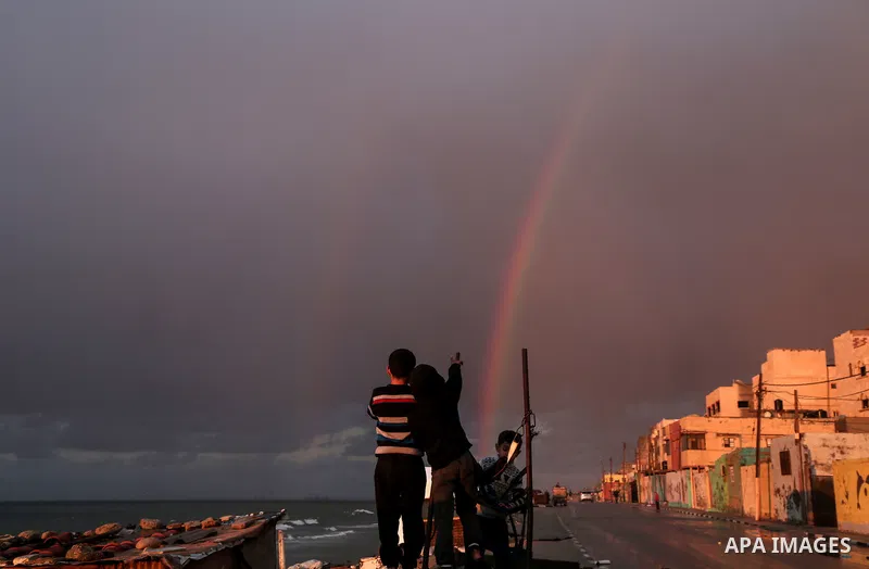 A picture taken on February 15, 2017 shows Palestinian children looking at a rainbow appearing over Al-Shati refugee camp in Gaza City. Photo by Mohammed Dahman