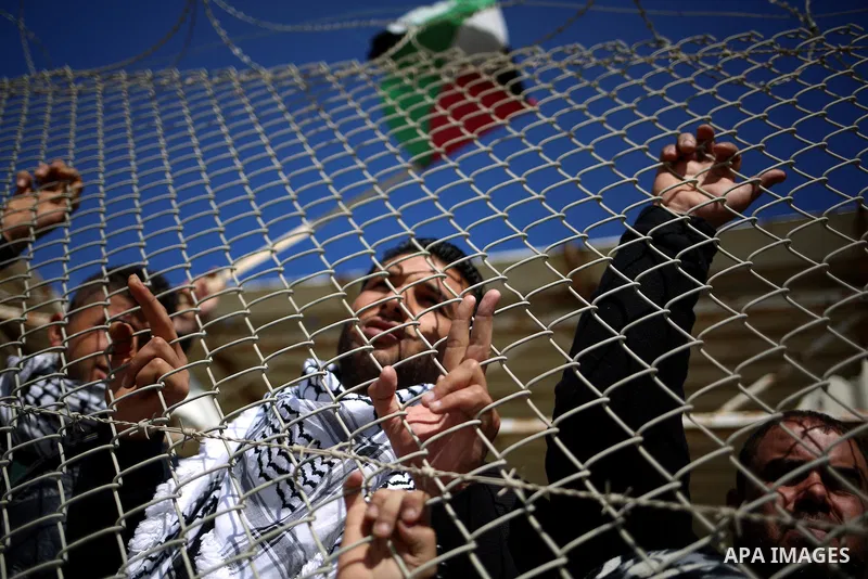 Palestinians stand behind a fence as they wait for the arrival of their relatives at Rafah crossing after it was opened by Egyptian authorities to allow stranded Palestinians to return to Gaza, in the southern Gaza Strip...