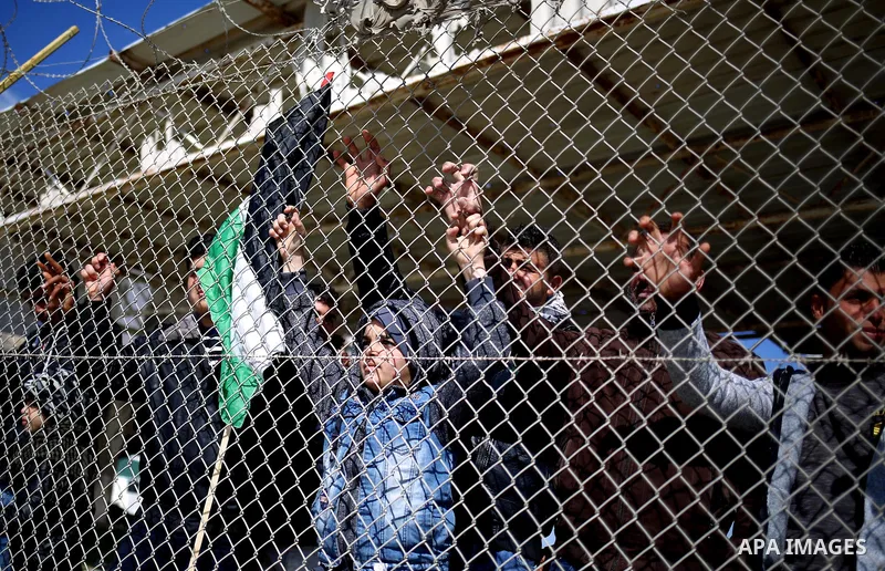 Palestinians stand behind a fence as they wait for the arrival of their relatives at Rafah crossing after it was opened by Egyptian authorities to allow stranded Palestinians to return to Gaza, in the southern Gaza Strip...