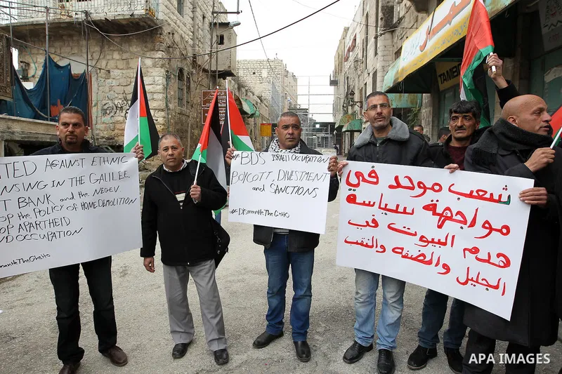 Palestinian protesters hold placards during a demonstration against the closure of Shuhada street, on the 23rd anniversary of the closure, on February 22, 2017 in the West Bank city of Hebron. On February 25, 1994 Israel...