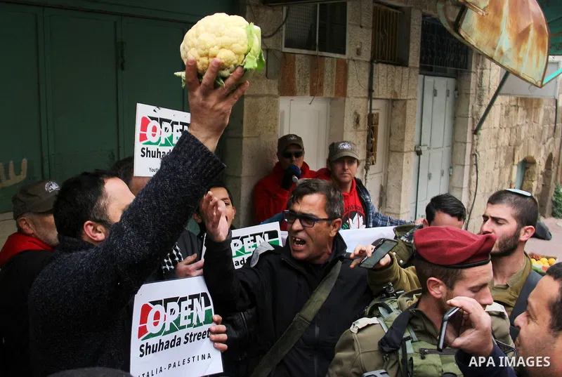 A Palestinian protester sells vegetables in front of Israeli Settlers during a demonstration against the closure of Shuhada street, on the 23rd anniversary of the closure, on February 22, 2017 in the West Bank city of He...