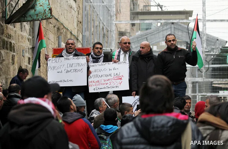 Palestinian protesters hold placards during a demonstration against the closure of Shuhada street, on the 23rd anniversary of the closure, on February 22, 2017 in the West Bank city of Hebron. On February 25, 1994 Israel...