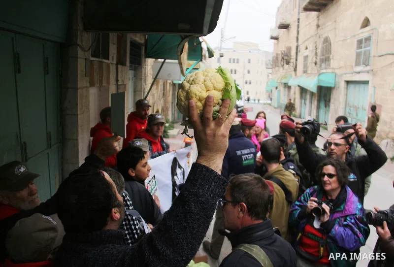 A Palestinian protester sells vegetables in front of Israeli Settlers during a demonstration against the closure of Shuhada street, on the 23rd anniversary of the closure, on February 22, 2017 in the West Bank city of He...