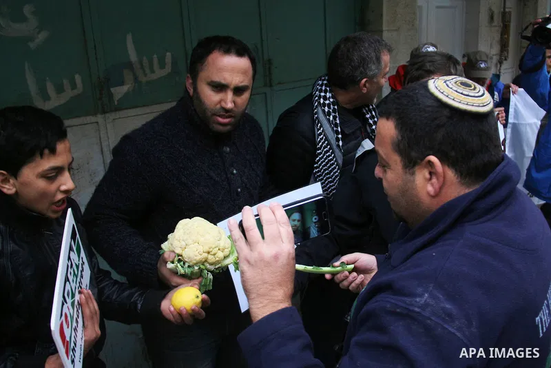 A Palestinian protester sells vegetables in front of Israeli Settlers during a demonstration against the closure of Shuhada street, on the 23rd anniversary of the closure, on February 22, 2017 in the West Bank city of He...