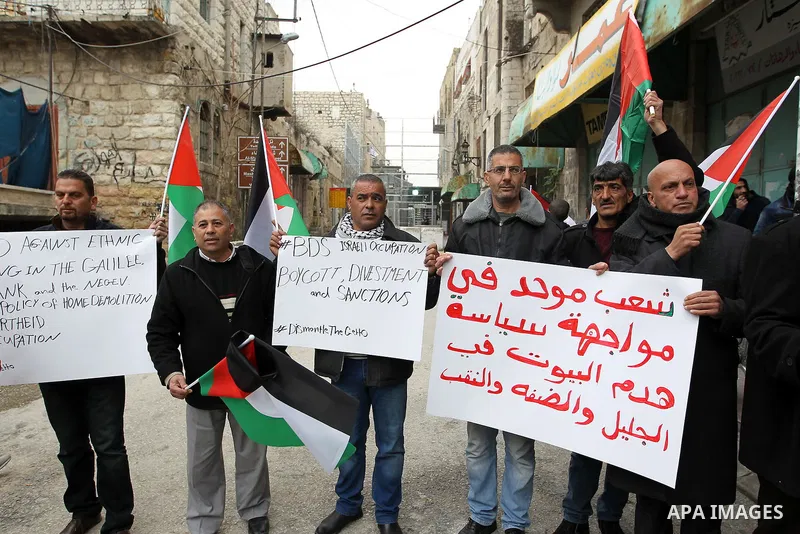 Palestinian protesters hold placards during a demonstration against the closure of Shuhada street, on the 23rd anniversary of the closure, on February 22, 2017 in the West Bank city of Hebron. On February 25, 1994 Israel...