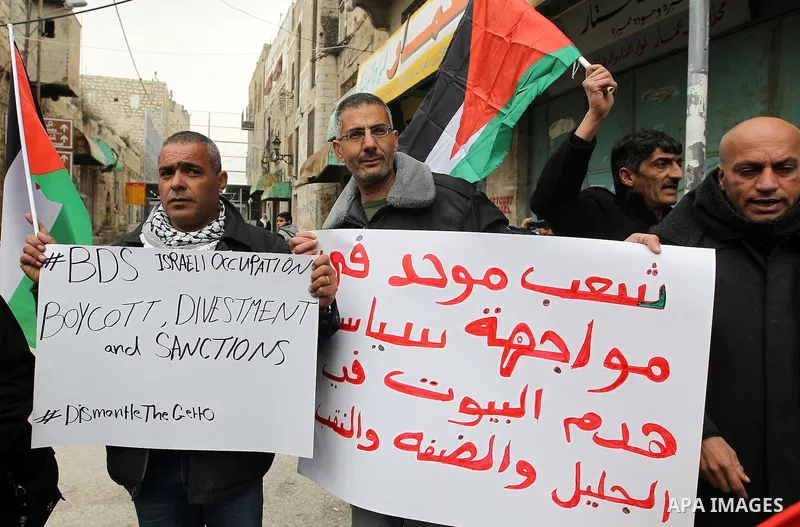 Palestinian protesters hold placards during a demonstration against the closure of Shuhada street, on the 23rd anniversary of the closure, on February 22, 2017 in the West Bank city of Hebron. On February 25, 1994 Israel...