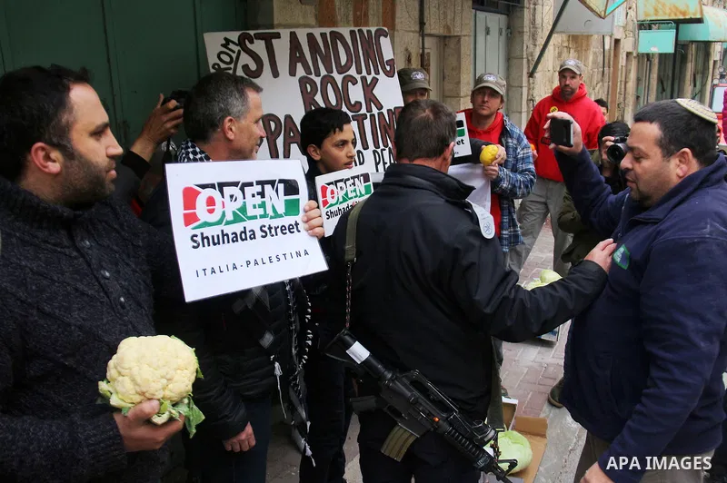 A Palestinian protester sells vegetables in front of Israeli Settlers during a demonstration against the closure of Shuhada street, on the 23rd anniversary of the closure, on February 22, 2017 in the West Bank city of He...