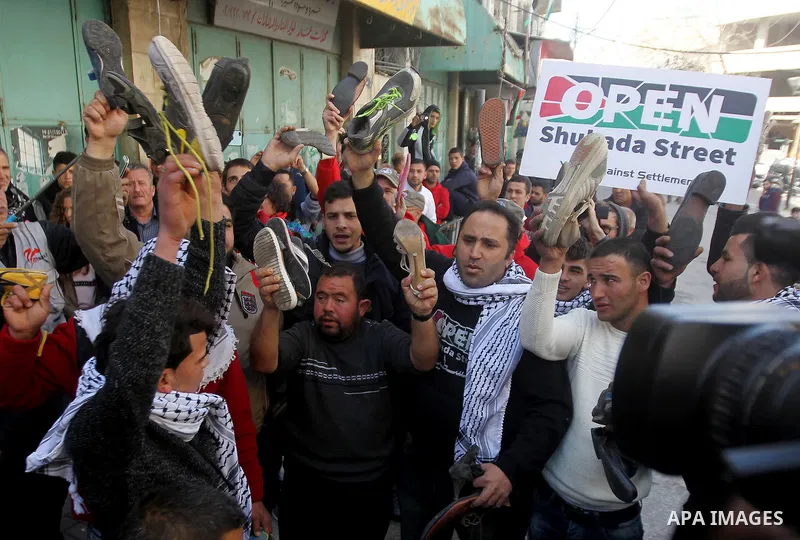 Palestinian demonstrators hold up old shoes before throwing them on a poster of US President Donald Trump as they protest against his support of Israel and demand for the Israeli army to re-open Shuhada Street, which is...