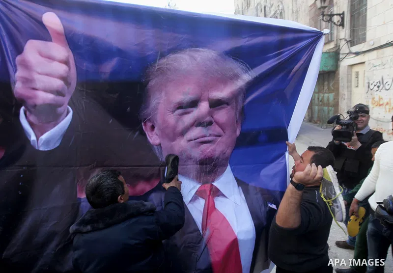 Palestinian demonstrators throw old shoes at a poster of US President Donald Trump as they protest against his support of Israel and demand for the Israeli army to re-open Shuhada Street, which is largely closed off to P...
