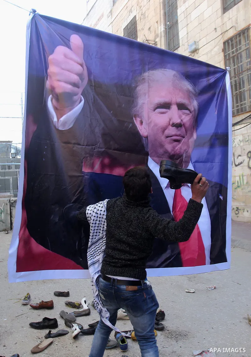 A Palestinian demonstrator throws an old shoe at a poster of US President Donald Trump as they protest against his support of Israel and demand for the Israeli army to re-open Shuhada Street, which is largely closed off...