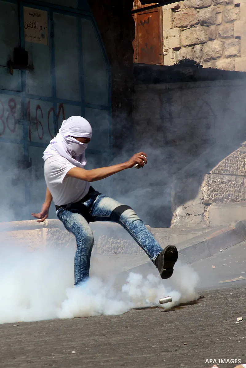 A Palestinian protester kicks a tear gas canister fired by Israeli security forces during clashes calling for the opening of Shuhada Street, which is largely closed off to Palestinians, in the West Bank city of Hebron, c...