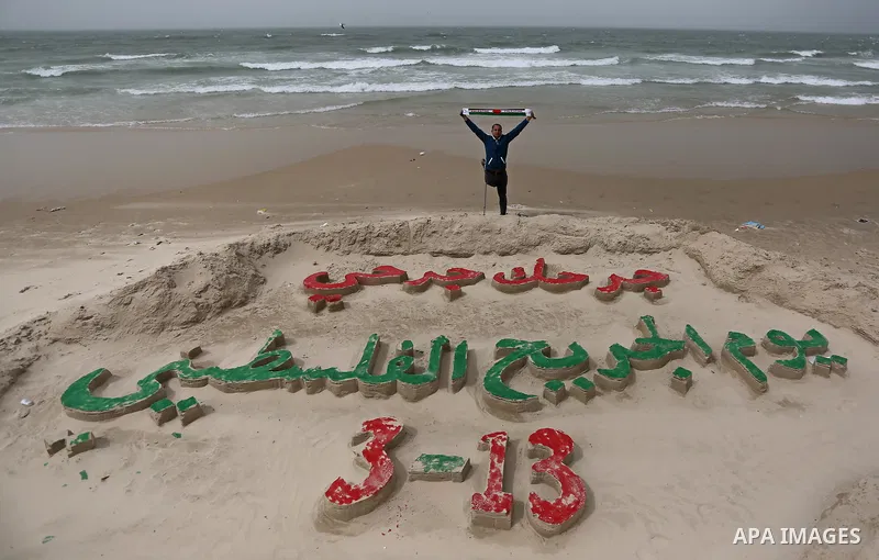 A Palestinian artist Mohammed Totah with amputated leg poses for a picture behind a sand sculpture to mark the Palestinian Wounded's Day in Gaza City, on March 12, 2017. Photo by Ashraf Amra