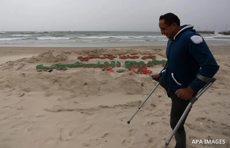 A Palestinian artist Mohammed Totah with amputated leg poses for a picture behind a sand sculpture to mark the Palestinian Wounded's Day in Gaza City, on March 12, 2017. Photo by Ashraf Amra
