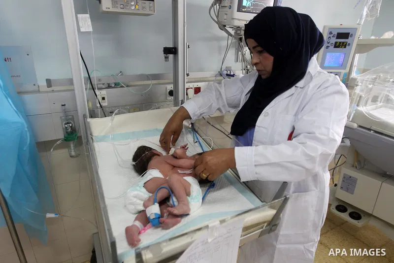 A Palestinian nurse checks on a One-day-old Palestinian conjoined twin boys lie in an incubator at the nursery Hospital in the West Bank city of Hebron, March 16, 2017. Photo by Wisam Hashlamoun