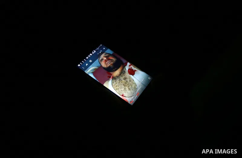 A Palestinian man watches a photo of the body of Hamas official, Mazen Faqha who was shot dead by gunmen in the Gaza Strip at his phone in Gaza City on March 24, 2017. Faqha was released along with more than 1,000 other...