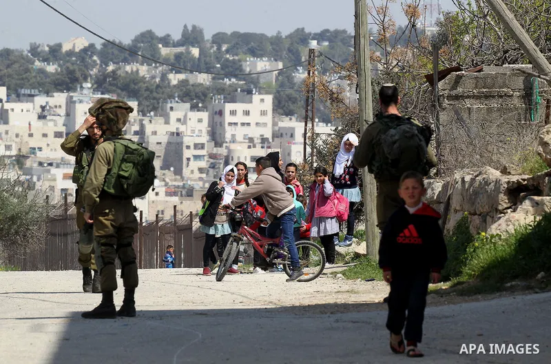 Palestinian students walk past Israeli soldiers in the West Bank city of Hebron March 26, 2017. Photo by Wisam Hashlamoun