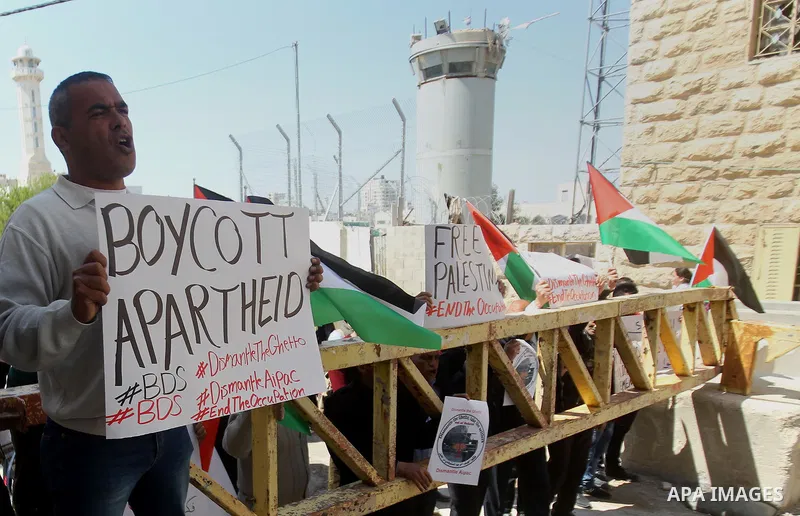 Palestinian demonstrators hold national flags and placards during a protest against Jewish settlements in the West Bank city of Hebron March 26, 2017. Photo by Wisam Hashlamoun