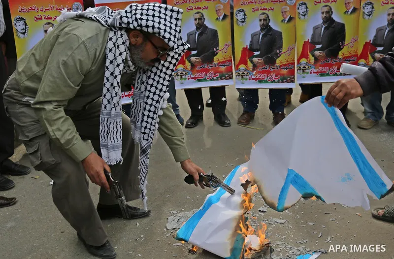 A Palestinian man burns an Israeli flag during a protest denouncing an assassination of Hamas official, Mazen Faqha who was freed by Israel in a 2011 prisoner swap after he was shot dead by unknown gunmen, in front of Re...