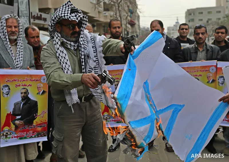 A Palestinian man burns an Israeli flag during a protest denouncing an assassination of Hamas official, Mazen Faqha who was freed by Israel in a 2011 prisoner swap after he was shot dead by unknown gunmen, in front of Re...