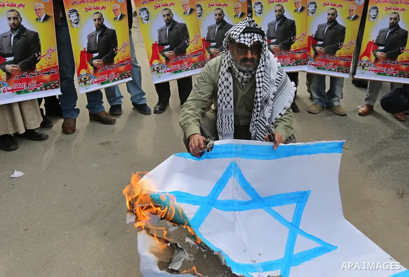 A Palestinian man burns an Israeli flag during a protest denouncing an assassination of Hamas official, Mazen Faqha who was freed by Israel in a 2011 prisoner swap after he was shot dead by unknown gunmen, in front of Re...