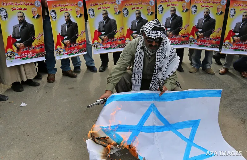 A Palestinian man burns an Israeli flag during a protest denouncing an assassination of Hamas official, Mazen Faqha who was freed by Israel in a 2011 prisoner swap after he was shot dead by unknown gunmen, in front of Re...