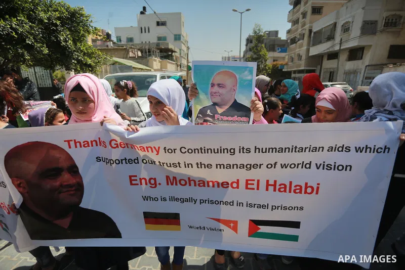 Palestinians hold posters of Mohammad El Halabi, World Vision's manager of operations in Gaza who was accused by Israel of funnelling millions of dollars in aid money to Hamas, during a protest in solidarity with El Hala...